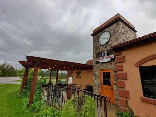 A rustic bar house with a stone clock tower, outdoor seating, and a cloudy sky in the background.
