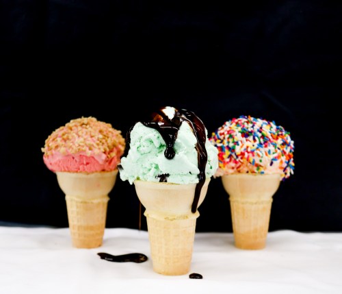 Three ice cream cones: pink, mint green with chocolate drizzle, and rainbow sprinkles, set against a black background.