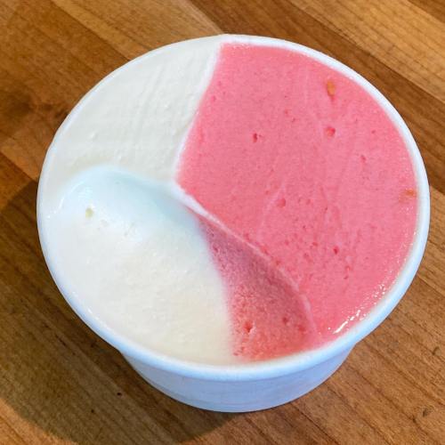 A cup of ice cream with three sections: white, pink, and a mix of both, on a wooden surface.