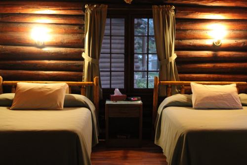 Cozy log cabin interior with two beds, soft lighting, and a window overlooking nature.