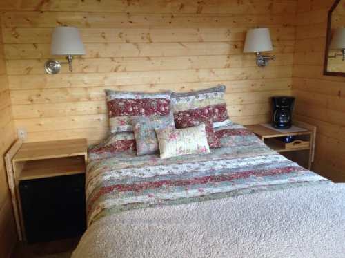 Cozy bedroom with a wooden wall, a floral quilted bed, bedside tables, and a coffee maker.