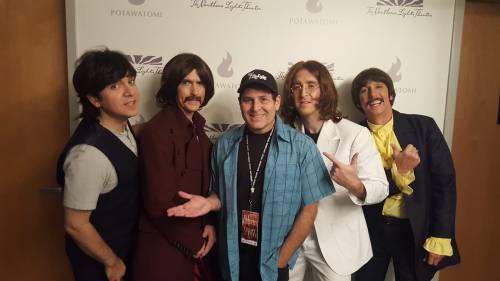 A group of five men dressed as The Beatles, posing together in front of a theater backdrop.