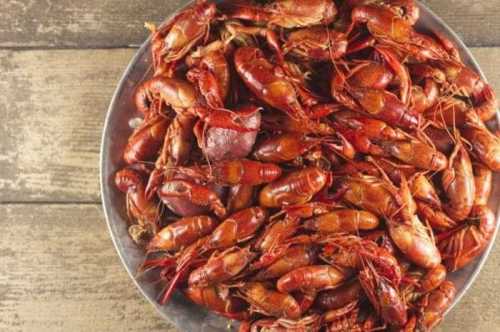 A metal platter filled with cooked crawfish, showcasing their vibrant red color against a rustic wooden background.