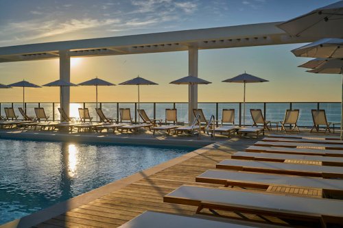 A serene poolside scene at sunset, featuring lounge chairs and umbrellas overlooking the ocean.