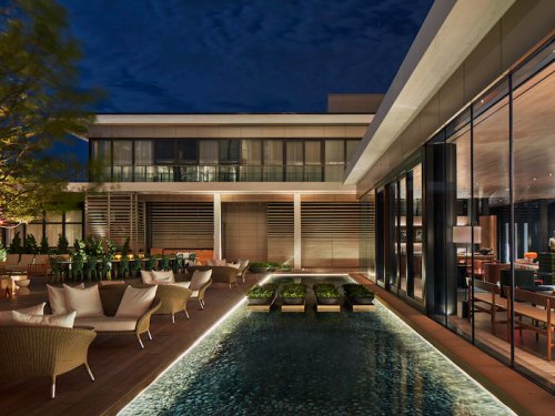 A modern outdoor lounge area at night, featuring seating, a pool, and stylish architecture illuminated by soft lighting.