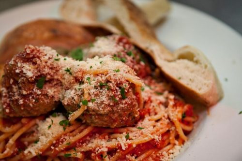A plate of spaghetti topped with meatballs, marinara sauce, grated cheese, and a side of bread.