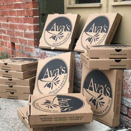 A stack of pizza boxes from Ava's Pizzeria and Wine Bar, leaning against a brick wall.