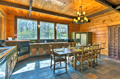 Cozy wooden kitchen with a dining table, chairs, large windows, and modern appliances, surrounded by nature.