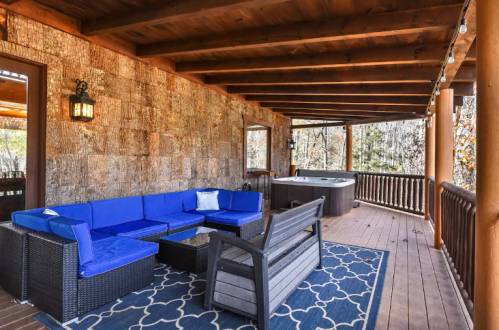 Cozy outdoor patio with blue seating, a coffee table, and a hot tub, surrounded by wooden beams and nature.