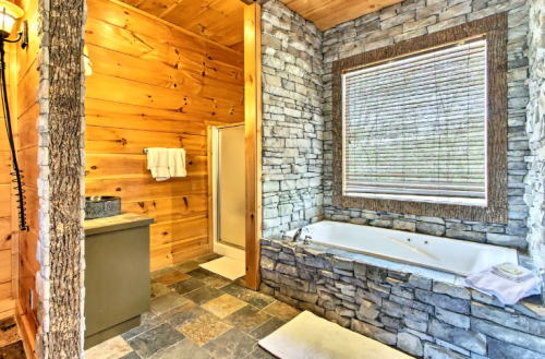 Cozy bathroom featuring a stone wall, wooden accents, a shower, and a jetted tub with natural light from a window.