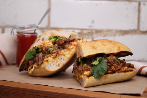 Two delicious sandwiches filled with meat, herbs, and toppings, served with a small jar of sauce on the side.