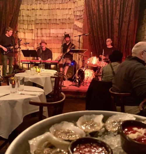 A cozy restaurant scene with a live band performing and a platter of oysters in the foreground.