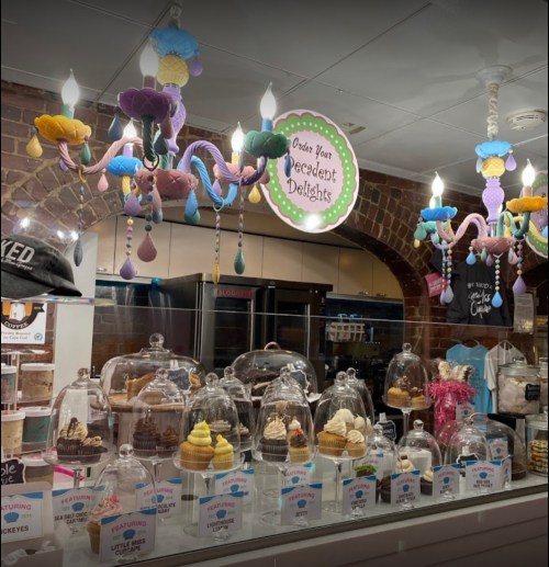 A colorful dessert shop display featuring various cupcakes and ice cream under glass domes, with whimsical chandeliers above.