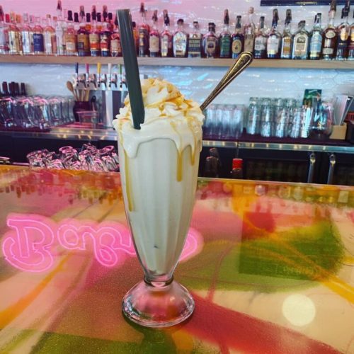 A tall glass of milkshake topped with whipped cream and caramel, set on a colorful bar counter.