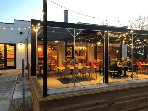 Outdoor dining area with string lights, colorful chairs, and tables, creating a cozy atmosphere at dusk.