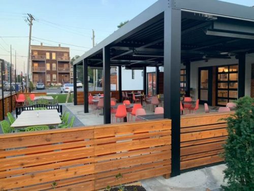 Outdoor dining area with modern furniture, featuring red chairs and wooden fences, set in an urban environment.