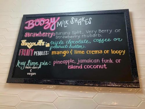 Menu board featuring colorful options for boozy milkshakes: strawberry, chocolate, fruity pebbles, and key lime pie.