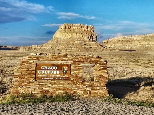 Sign for Chaco Culture National Historical Park, with a rocky mesa and blue sky in the background.