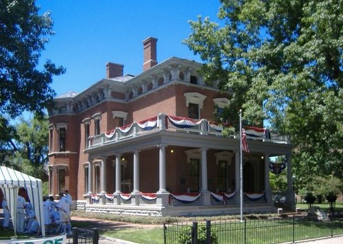 Historic brick mansion with decorative bunting, surrounded by trees and a clear blue sky.