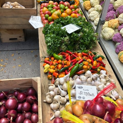 A vibrant display of fresh vegetables, including garlic, peppers, and various colorful tomatoes, in wooden crates.