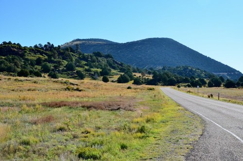 A winding road leads through a grassy landscape with rolling hills and clear blue skies in the background.
