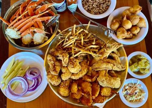 A large platter of fried seafood, including shrimp and fish, with sides of crab, fries, and various condiments.