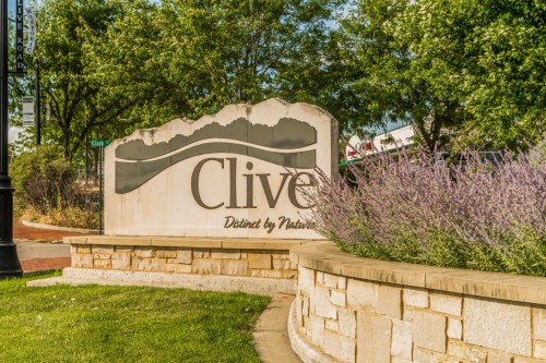 Sign for Clive, Iowa, featuring the text "Clive" and "Distinct by Nature," surrounded by greenery and flowers.
