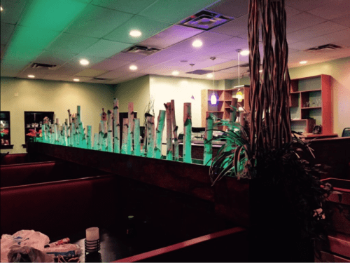 A restaurant interior featuring a bar with decorative wooden elements and green lighting, surrounded by seating areas.
