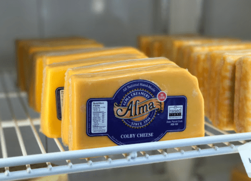 Blocks of Colby cheese with a blue label on a shelf in a refrigerator.
