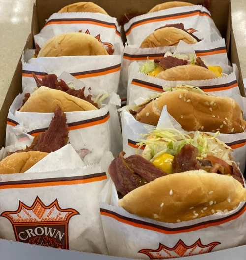 A box filled with several sandwiches wrapped in paper, featuring various toppings and meats.