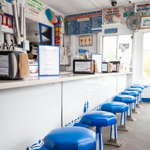 A bright ice cream shop interior with blue stools, a counter, and menus displayed on the walls.