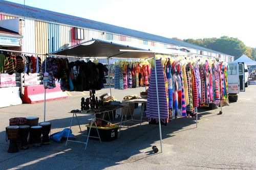 A vibrant market stall displaying colorful clothing and accessories, with drums and other items for sale in the foreground.