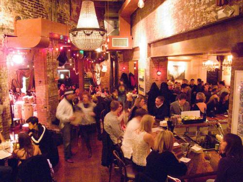 A lively restaurant scene with diners, a bar, and warm lighting, featuring a mix of people enjoying their evening.