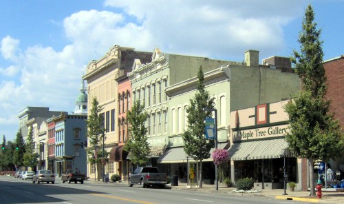 A charming street view of colorful historic buildings with trees and a gallery, under a blue sky with clouds.