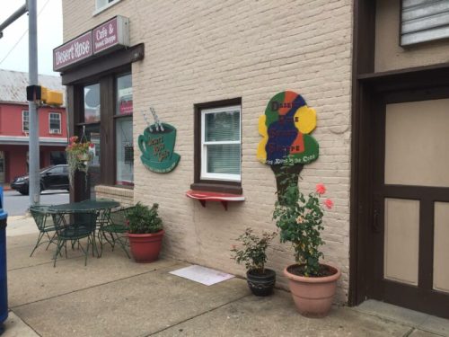 Exterior of a café with a sign, potted plants, and outdoor seating on a sidewalk.