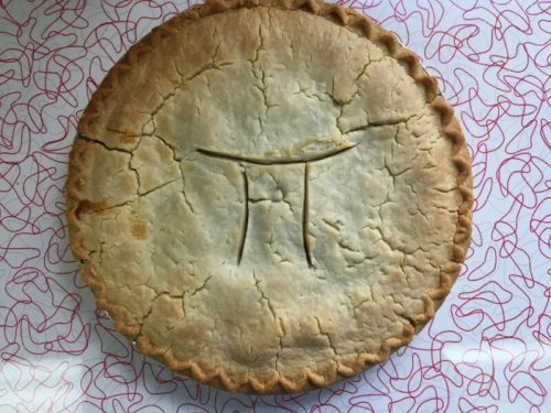 A round pie with a golden crust, featuring a carved design resembling the symbol for pi (π) on top.