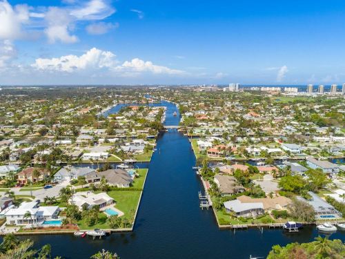 Aerial view of a coastal neighborhood with canals, homes, and boats under a clear blue sky.