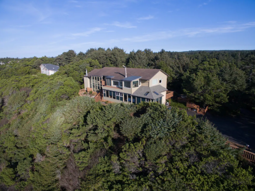 Aerial view of a modern house surrounded by lush greenery and trees, overlooking a scenic landscape.