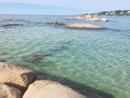 Calm turquoise waters with rocky outcrops and a distant shoreline under a clear blue sky.