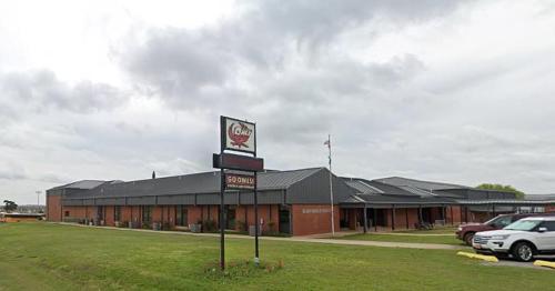 A brick building with a metal roof, featuring a sign and grassy area, under a cloudy sky.