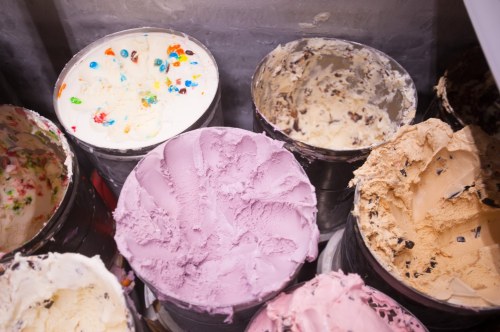 Various ice cream tubs with colorful flavors, including pink, beige, and white, in a freezer.