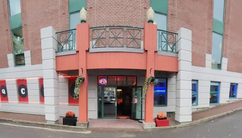 A modern building entrance with an "Open" sign, colorful windows, and decorative plants on either side.