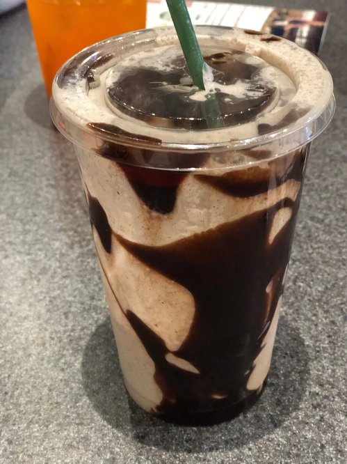 A plastic cup filled with a chocolate swirl drink topped with whipped cream and a green straw.