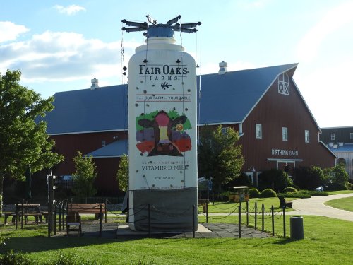 A large milk bottle sculpture stands in front of a red barn, surrounded by green grass and trees at Fair Oaks Farms.