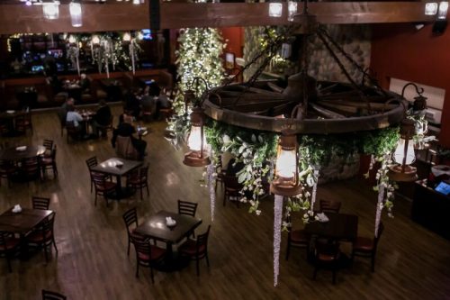 A cozy restaurant interior with wooden tables, a decorative chandelier, and festive greenery.