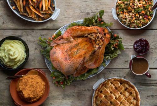 A festive Thanksgiving spread featuring a roasted turkey, stuffing, mashed potatoes, sweet potatoes, cranberry sauce, and pie.