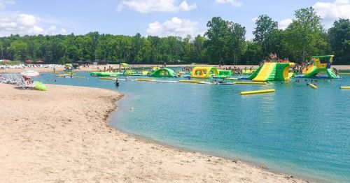 A sandy beach with a vibrant inflatable water park and people enjoying the water on a sunny day.