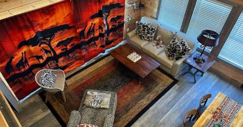 Cozy living room with animal-themed decor, vibrant curtains, a wooden table, and a mix of patterned furniture.