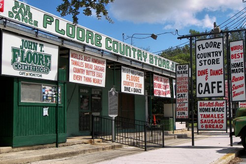 A colorful storefront with signs for Floore Country Store, featuring homemade tamales, sausage, and a café.