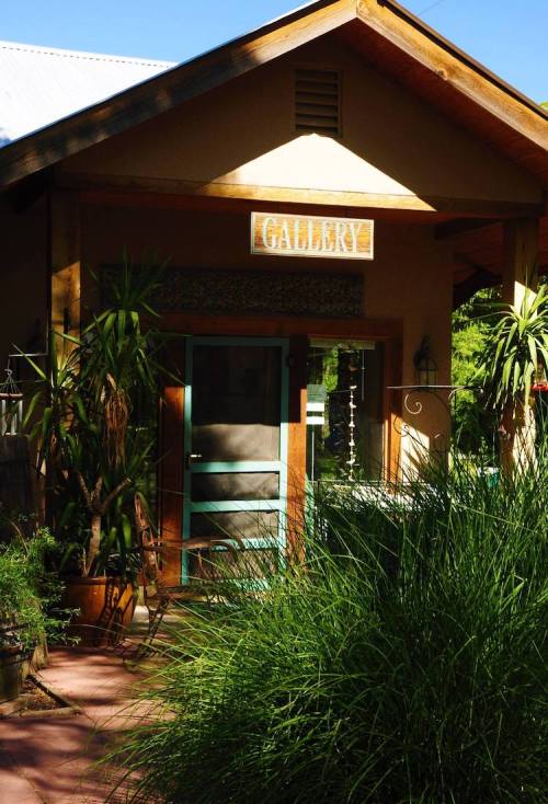 A cozy gallery entrance surrounded by lush greenery and plants, with a sign reading "GALLERY" above the door.